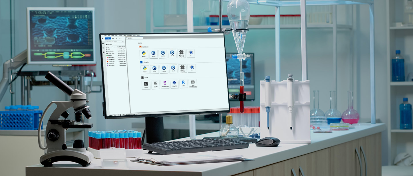 A laboratory workspace featuring a microscope and test tubes filled with blood on a counter next to a computer monitor displaying scientific software. The lab is equipped with scientific glassware, pipettes, and flasks containing colorful liquids. In the background, there is another screen showing a digital scientific interface, and laboratory equipment and chemical bottles are visible on shelves.
