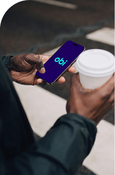 Obi Splash In Hand | Iterators A person standing outside, holding a smartphone showing the "obi" logo on the screen in one hand and a white disposable coffee cup in the other.